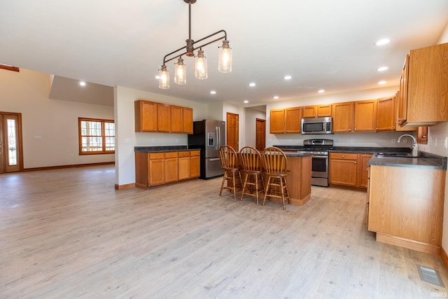 kitchen featuring a breakfast bar area, a kitchen island, a sink, appliances with stainless steel finishes, and light wood-type flooring