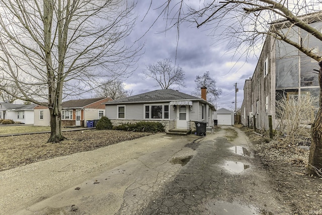 view of front of house with a detached garage, an outbuilding, a chimney, and driveway