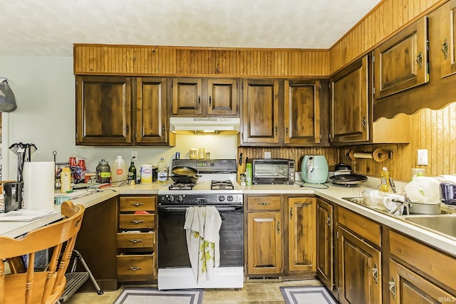 kitchen with under cabinet range hood, a sink, range with gas cooktop, a toaster, and light countertops