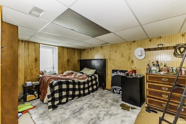 carpeted bedroom with a drop ceiling, visible vents, and wood walls