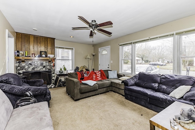 living area with a fireplace, a healthy amount of sunlight, a ceiling fan, and light carpet