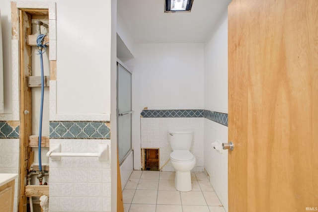 bathroom featuring tile patterned flooring, tile walls, a wainscoted wall, toilet, and vanity