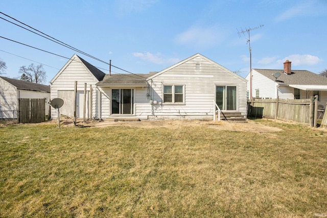 back of house with entry steps, a yard, fence, and a shingled roof