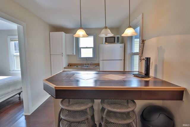 kitchen with a sink, stainless steel microwave, freestanding refrigerator, tile countertops, and a breakfast bar area