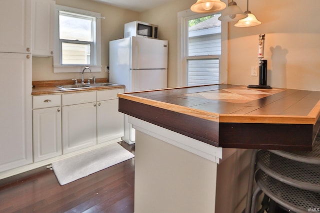 kitchen featuring wood finished floors, freestanding refrigerator, a sink, white cabinetry, and stainless steel microwave