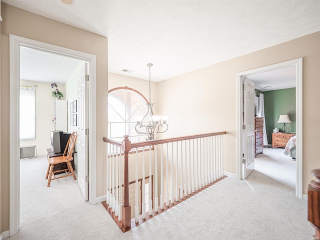 corridor featuring carpet, baseboards, visible vents, an upstairs landing, and a chandelier