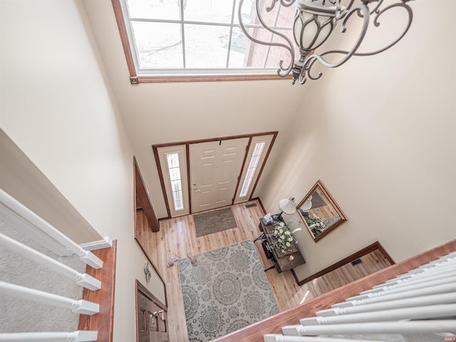 foyer entrance with an inviting chandelier, a towering ceiling, wood finished floors, and a wealth of natural light