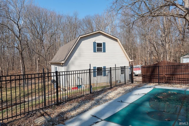 view of home's exterior with a gambrel roof, roof with shingles, and fence