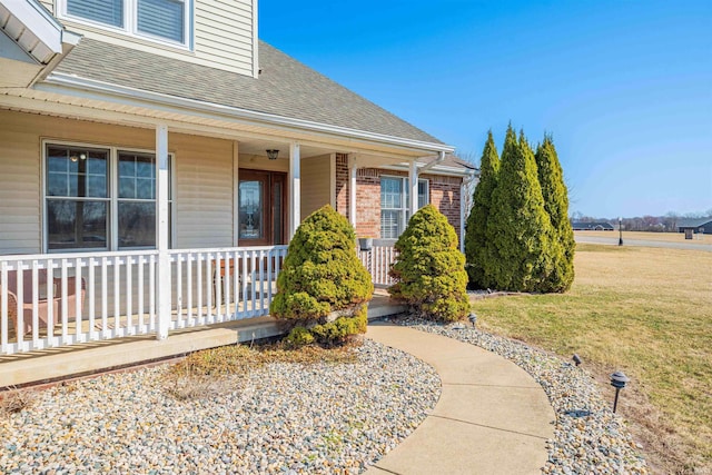 property entrance with a yard, roof with shingles, and a porch