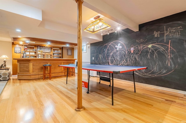 playroom featuring beamed ceiling, a bar, wood finished floors, and an accent wall