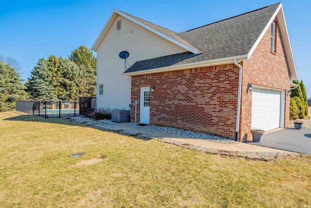 view of side of home featuring a fenced in pool, driveway, roof with shingles, a yard, and brick siding