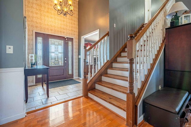 entryway featuring a notable chandelier, wood finished floors, baseboards, a towering ceiling, and stairs