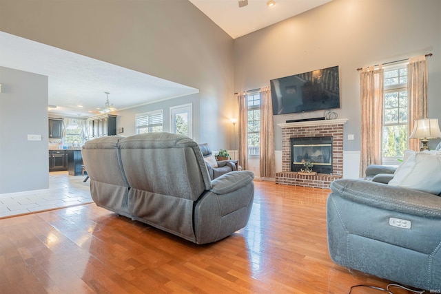 living area featuring a healthy amount of sunlight, a fireplace, light wood-type flooring, and a high ceiling