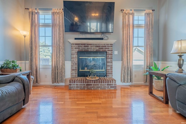 living area featuring a fireplace, wood finished floors, a healthy amount of sunlight, and a wainscoted wall