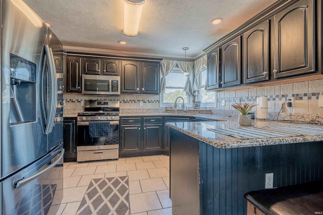 kitchen featuring light stone countertops, a peninsula, a sink, appliances with stainless steel finishes, and backsplash