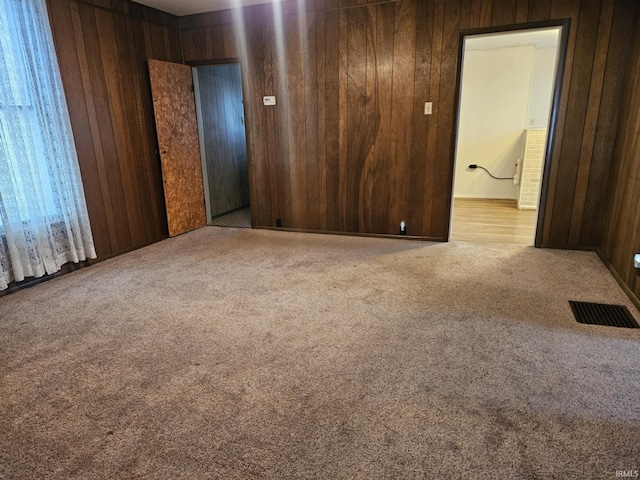 carpeted spare room featuring visible vents and wood walls