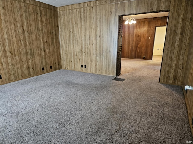 carpeted empty room with visible vents, wood walls, and a chandelier