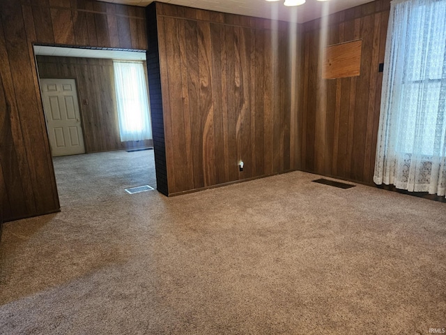 empty room featuring visible vents, wood walls, and carpet flooring