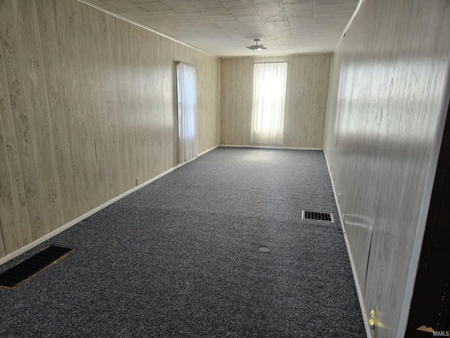 carpeted spare room with wooden walls, baseboards, and visible vents