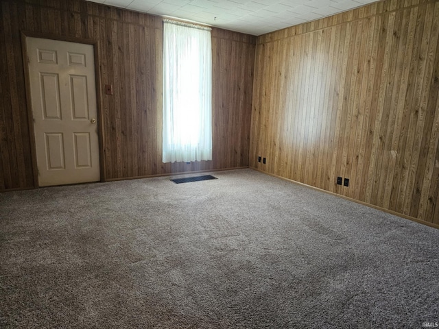 unfurnished room featuring visible vents, carpet floors, and wooden walls