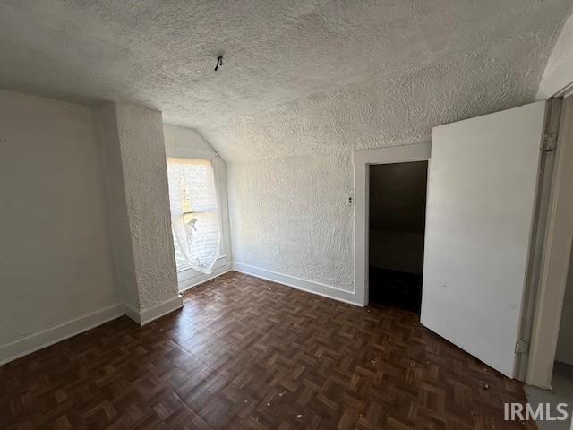 empty room with baseboards, a textured ceiling, lofted ceiling, and a textured wall