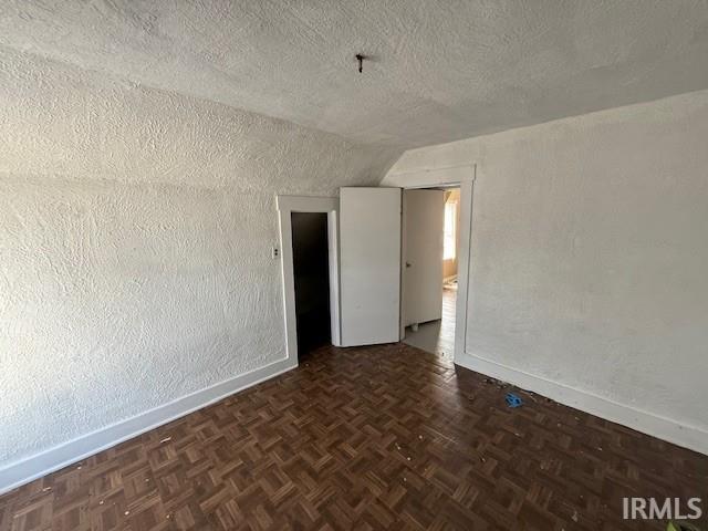 spare room with a textured wall, a textured ceiling, baseboards, and vaulted ceiling