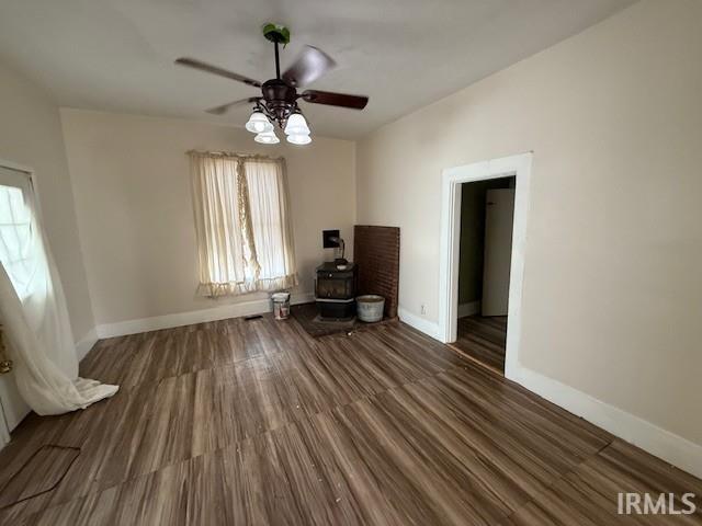 interior space featuring ceiling fan, baseboards, wood finished floors, and a wood stove