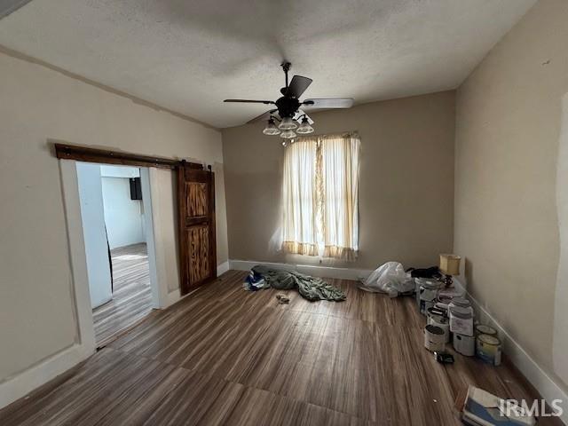 unfurnished room featuring a barn door, a ceiling fan, baseboards, and a textured ceiling