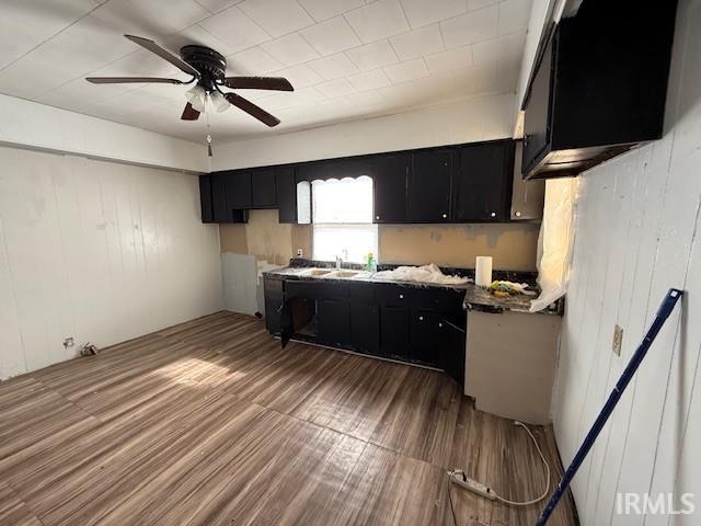 kitchen featuring wood walls, wood finished floors, ceiling fan, and dark cabinets