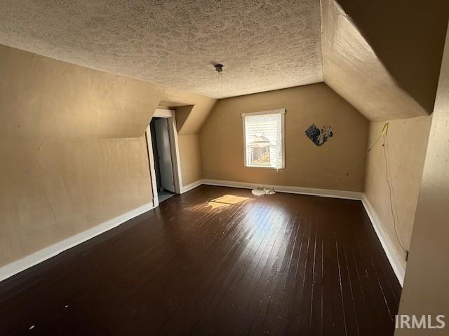 bonus room featuring lofted ceiling, baseboards, wood-type flooring, and a textured ceiling