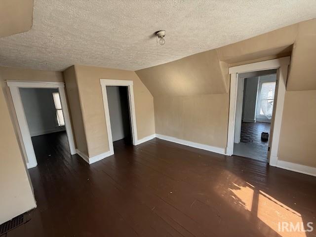 additional living space featuring baseboards, a textured ceiling, wood finished floors, and vaulted ceiling