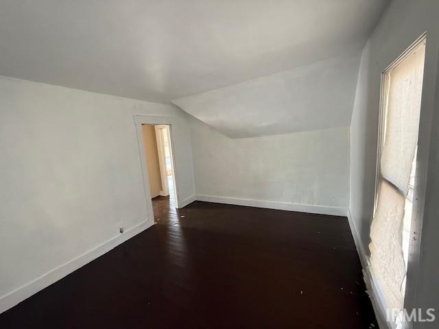 bonus room featuring lofted ceiling, baseboards, and dark wood-type flooring