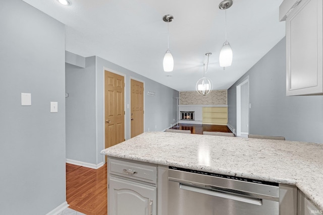 kitchen featuring stainless steel dishwasher, open floor plan, a glass covered fireplace, baseboards, and hanging light fixtures