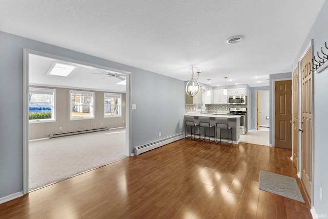 unfurnished living room with a ceiling fan, wood finished floors, visible vents, a baseboard radiator, and baseboard heating