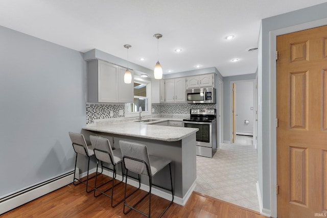 kitchen featuring stainless steel appliances, baseboard heating, a peninsula, and a breakfast bar area