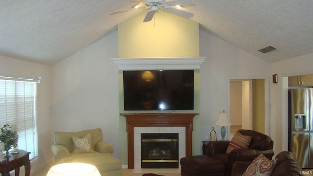 living area with visible vents, lofted ceiling, ceiling fan, and a tiled fireplace