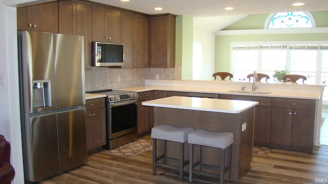 kitchen featuring dark wood-type flooring, a breakfast bar, vaulted ceiling, appliances with stainless steel finishes, and a sink