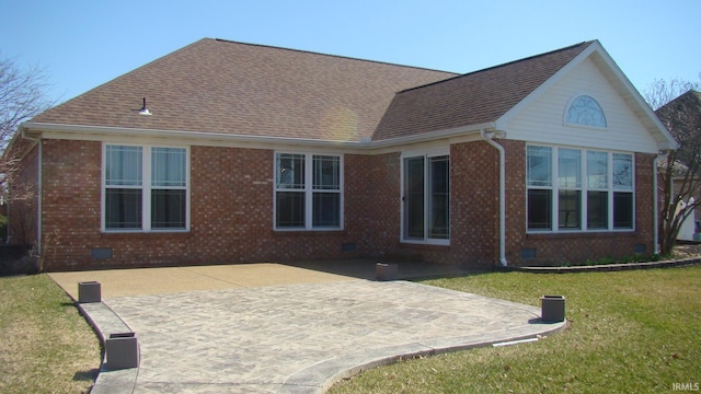 rear view of house with brick siding, roof with shingles, a lawn, crawl space, and a patio