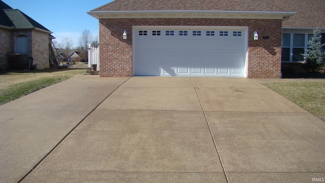 view of side of home with a garage, brick siding, concrete driveway, and a shingled roof