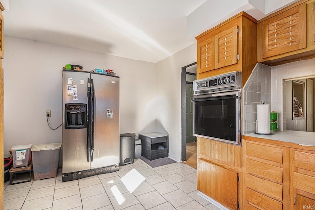 kitchen featuring light countertops, light tile patterned flooring, stainless steel fridge, and oven