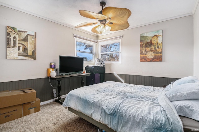 carpeted bedroom with a wainscoted wall, ornamental molding, and a ceiling fan