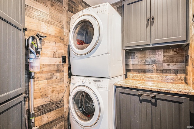 laundry room with cabinet space, wood walls, and stacked washing maching and dryer