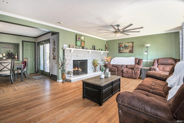 living area featuring light wood finished floors, baseboards, ceiling fan, ornamental molding, and a stone fireplace