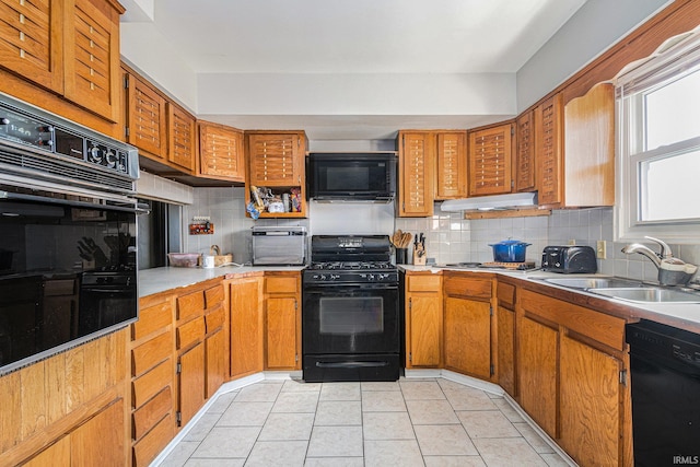 kitchen featuring light tile patterned flooring, a sink, decorative backsplash, black appliances, and under cabinet range hood