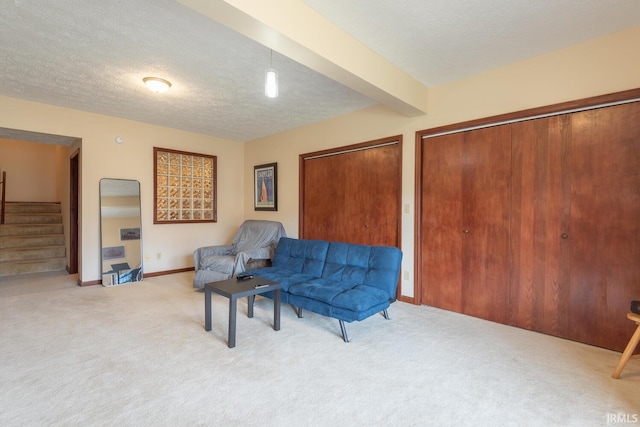 living area featuring baseboards, beamed ceiling, stairs, carpet floors, and a textured ceiling