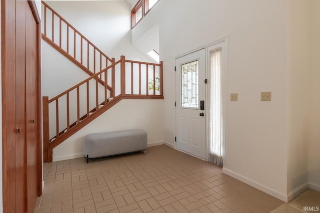 entryway featuring brick floor, stairs, baseboards, and a towering ceiling