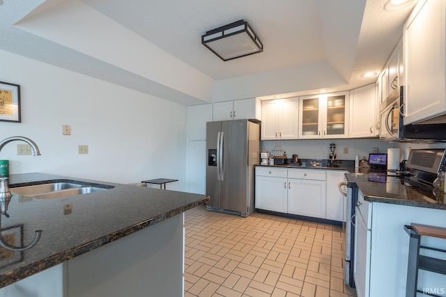 kitchen featuring brick patterned floor, a sink, white cabinetry, appliances with stainless steel finishes, and glass insert cabinets