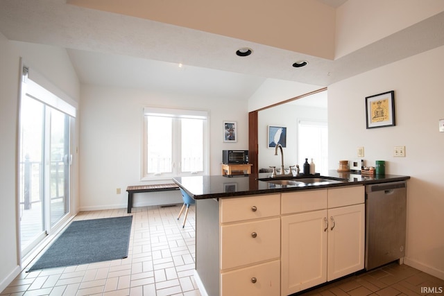 kitchen with a sink, dark stone counters, a peninsula, dishwasher, and vaulted ceiling