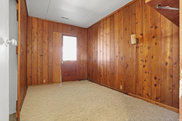 carpeted spare room featuring visible vents and wooden walls