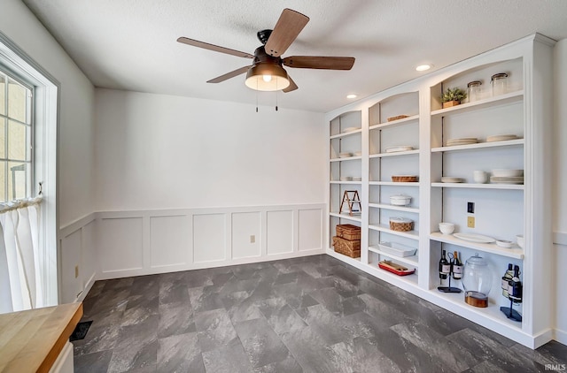 spare room featuring built in features, wainscoting, a ceiling fan, and a decorative wall